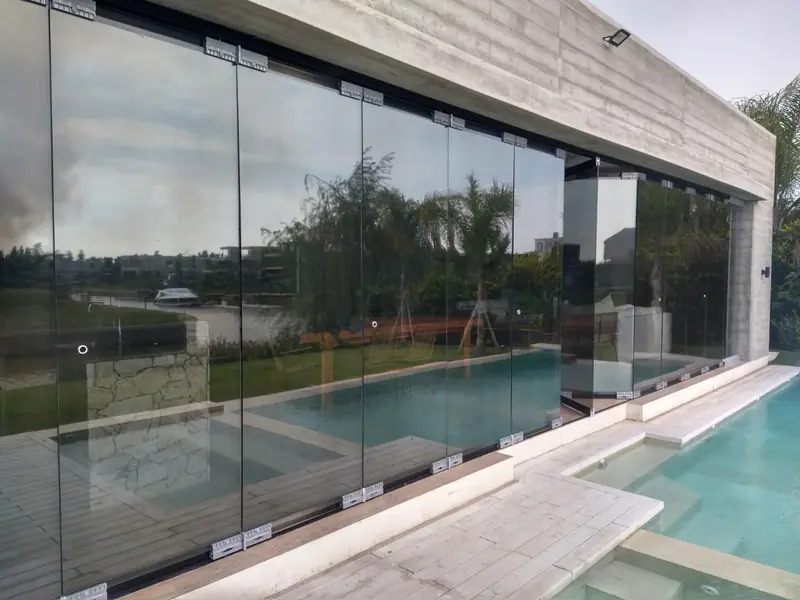 Fachada vidriada con efecto espejo junto a una pileta